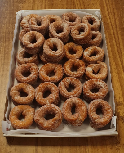 Bandeja rectangular con rosquillas fritas cubiertas de azúcar, dispuestas en filas sobre papel encerado, sobre una mesa de madera.